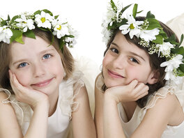 Zwei Mädchen in weißen Kleidern und mit Blumenkränzen aus weißen Blumen, liegend, die Hände an die Wangen gelegt