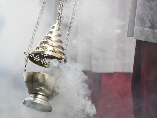 Weihrauchnebel aus einem Weihrauchschwenker. Am Rand rot-weiße Gewänder.